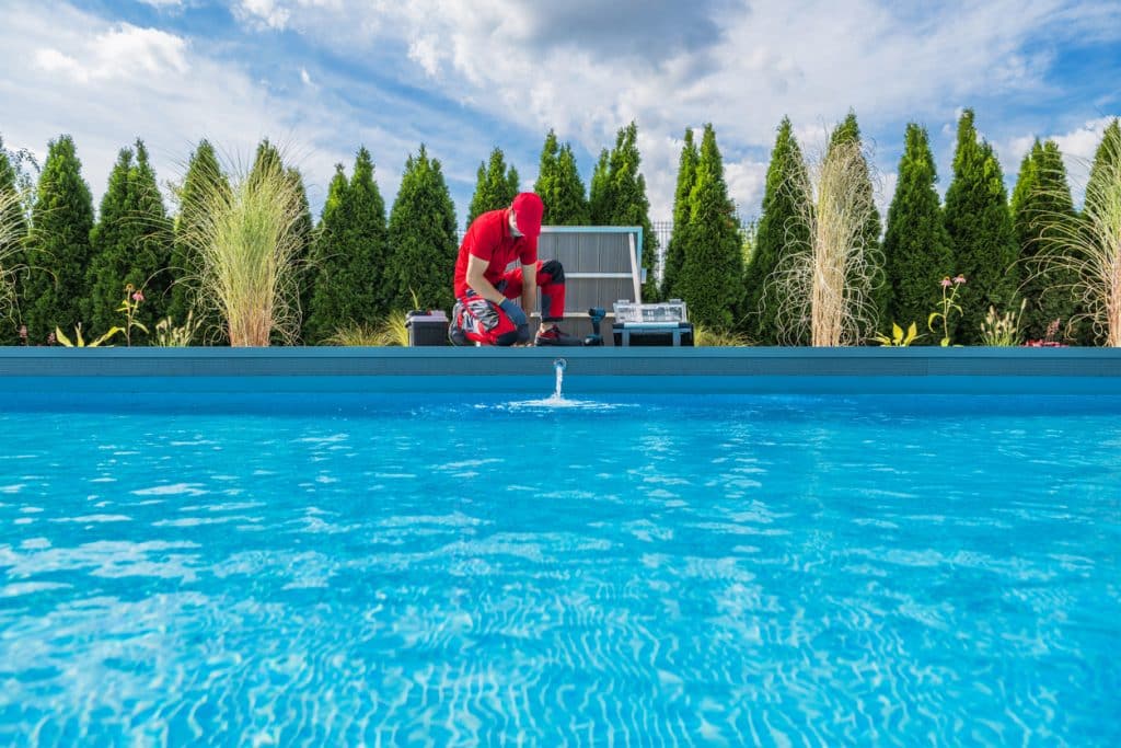 Pool technician performing maintenance on a residential swimming pool with tools and equipment beside the pool.